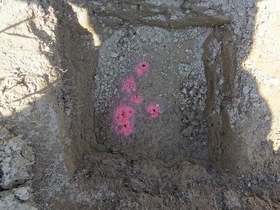 Eine Bodengrube - an deren Grund sind mind, sechs größere Löcher mit pinker Sprühfarbe markiert.