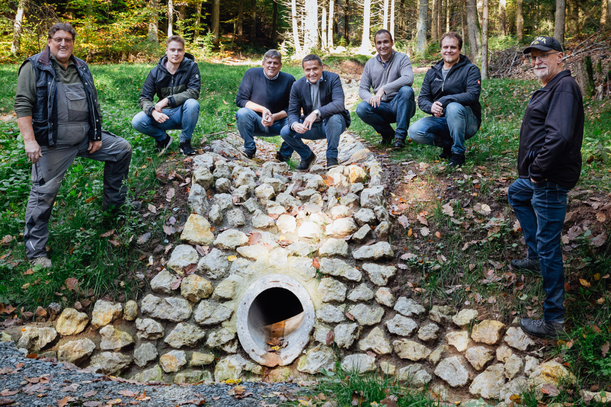 eine Gruppe Menschen steht/hockt auf einer Steinschüttung mit Rohrauslass; im Hintergrund ist die umgestaltete Tiefenlinie mit Sohlschwellen zu sehen