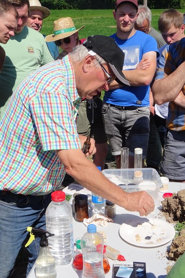 Max Stadler träufelt auf seinem Versuchstisch auf dem Feld Salzsäure auf verschiedene Kalkdüngerproben auf einem Pappteller. Die meisten schäumen deutlich.