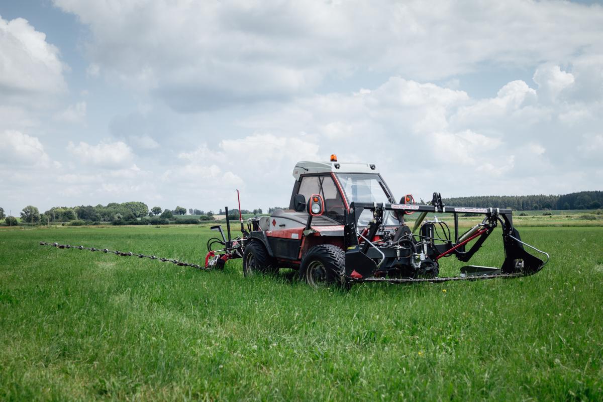 Ein Lader mit Front- und Seitenmähbalken in Leichtbauweise auf einer Wiese. Der Frontmähbalken hat eine Art Auffangkorb