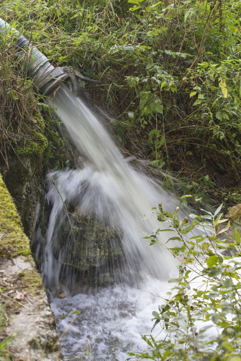 Aus einem C-Rohr fließt Wasser in einen Bach.