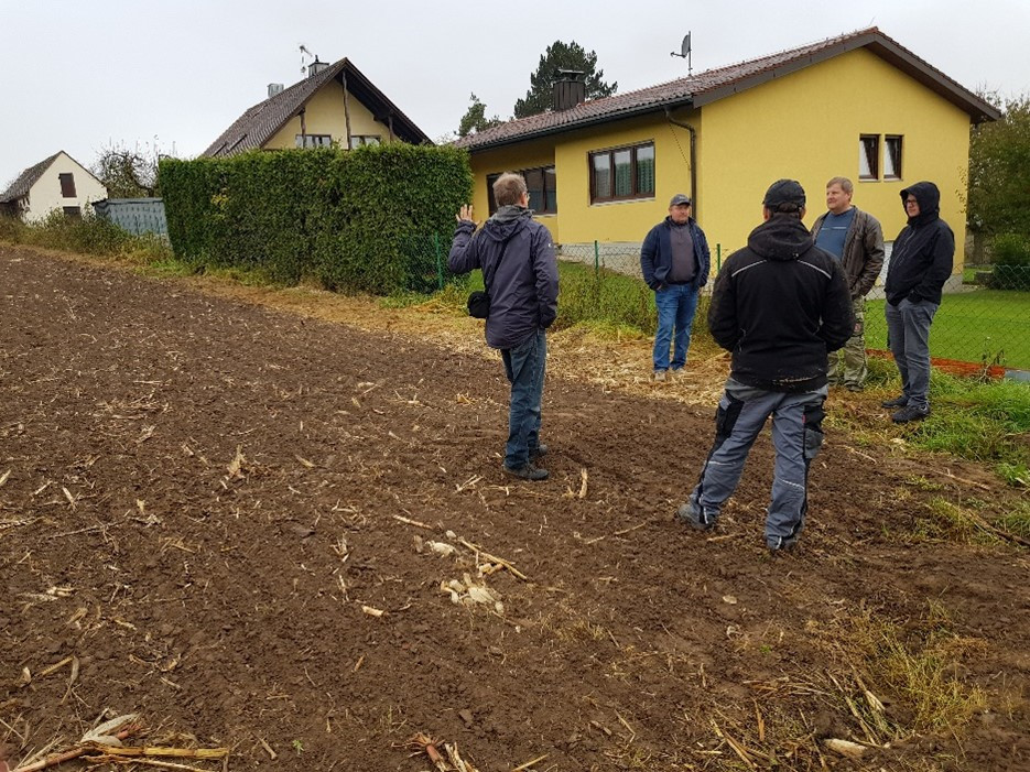 Foto: Eine Gruppe von Menschen steht auf einem abgeernteten Maisacker