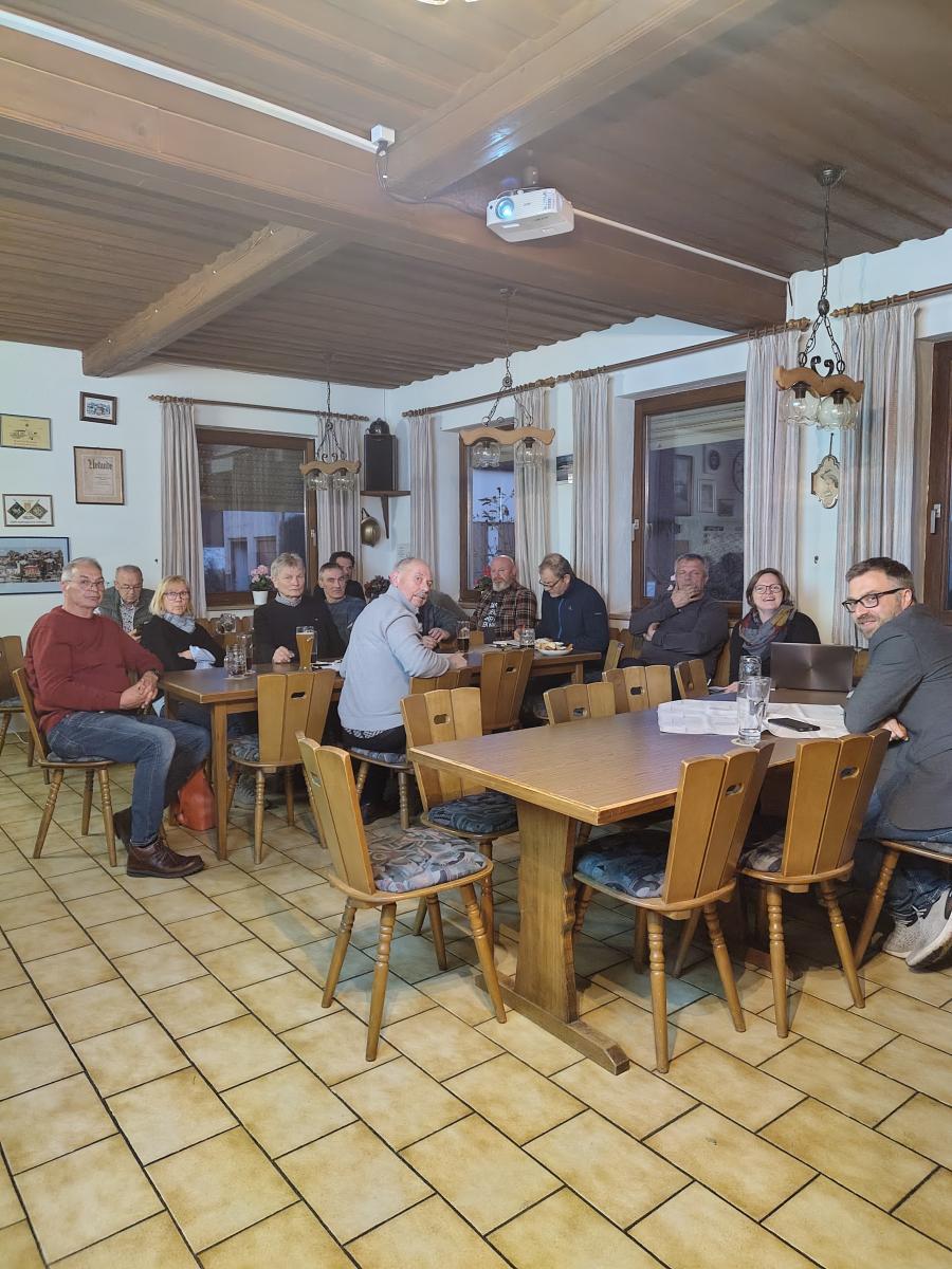 Foto: in einem rustikalen Raum sitzen an Tischen mehrere Männer und Frauen