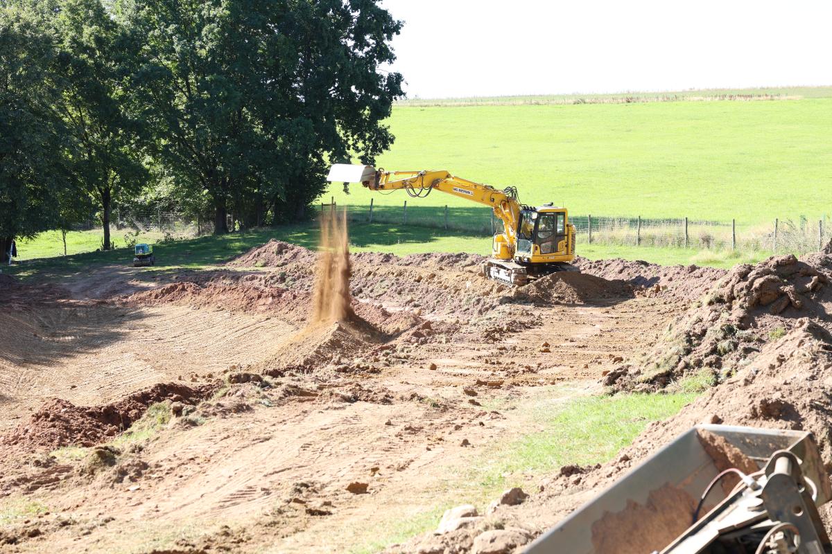 Ein Bagger steht am Rand eines neu gebauten Teiches und baut Bodenaushub ein