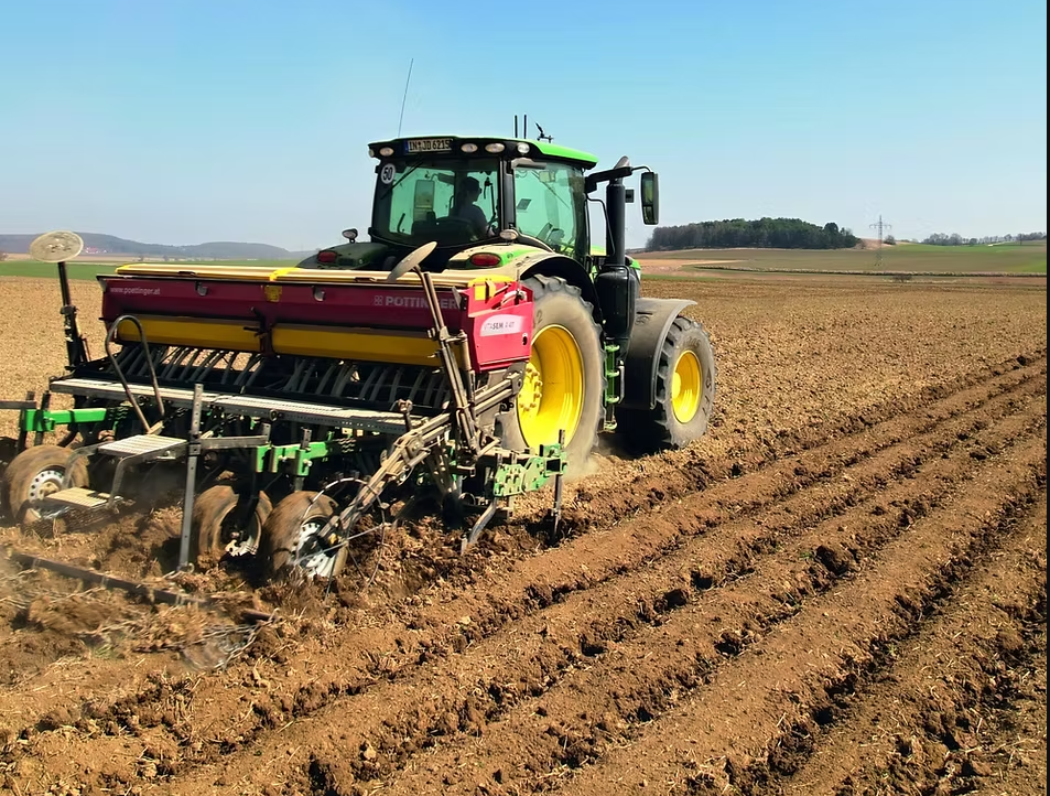 Ein John Deere mit Turiel-Sämaschine produziert flache Dämme auf einem ebenen, ockerbraunen Acker