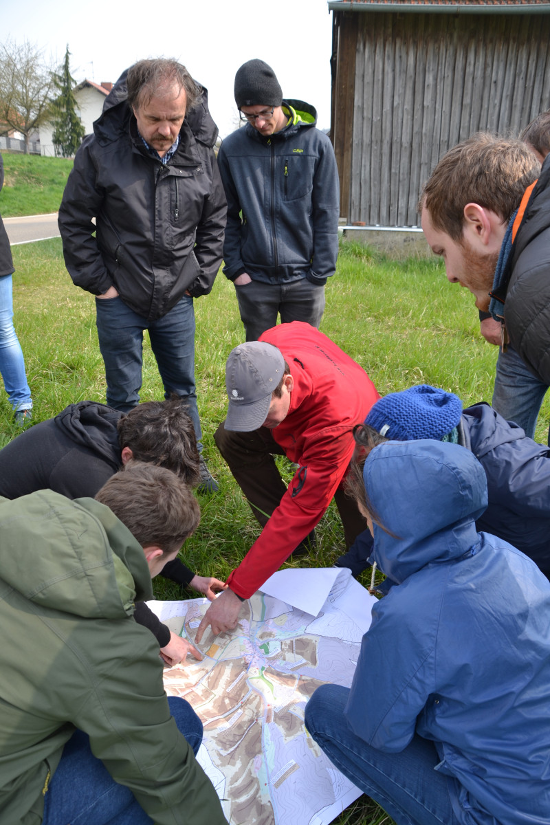 Eine Gruppe Menschen steckt im Freien die Köpfe über einer Karte zusammen
