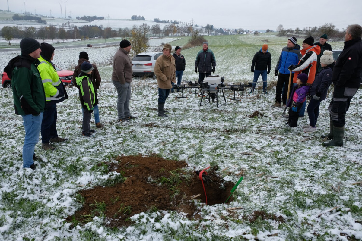 Foto: Personengruppe auf einem Feld mit Zwischenfrüchten, eine Agrardrohne befindet sich in der Bildmitte