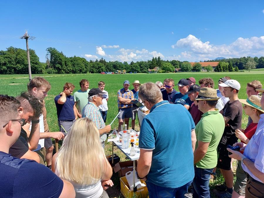 Zahlreiche Menschen bei bestem Wetter auf einem Feld - in der Mitte ein Tisch mit Utensilien zur chemischen Analyse