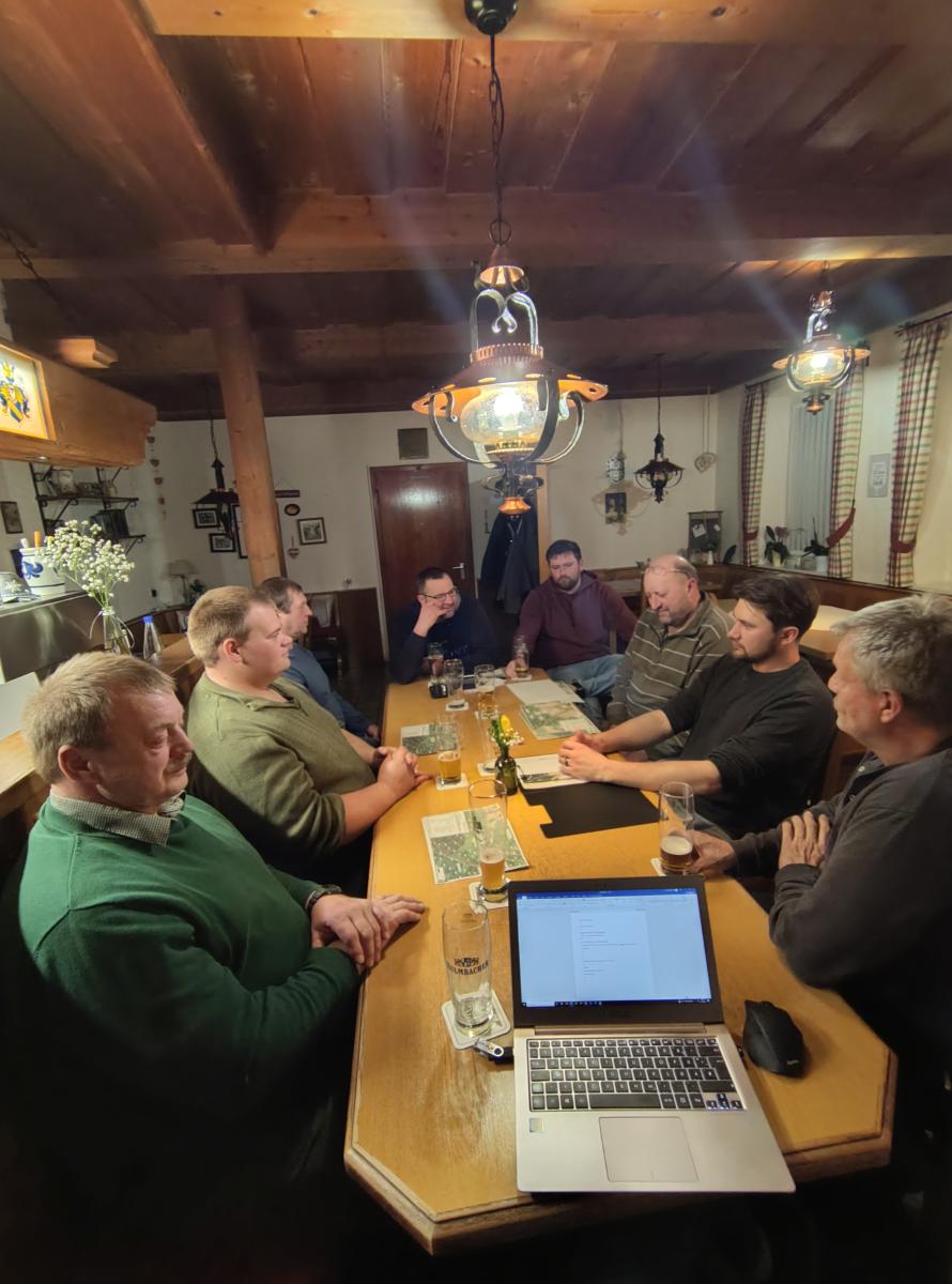 Foto: in einer rustikalen Gastwirtschaft sitzen 8 Männer um einen Tisch.