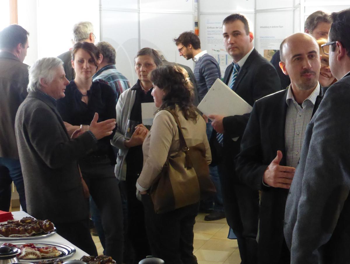 Viele Menschen unterhalten sich angeregt in einem Raum. Im Hintergrund gibt es Stellwände.