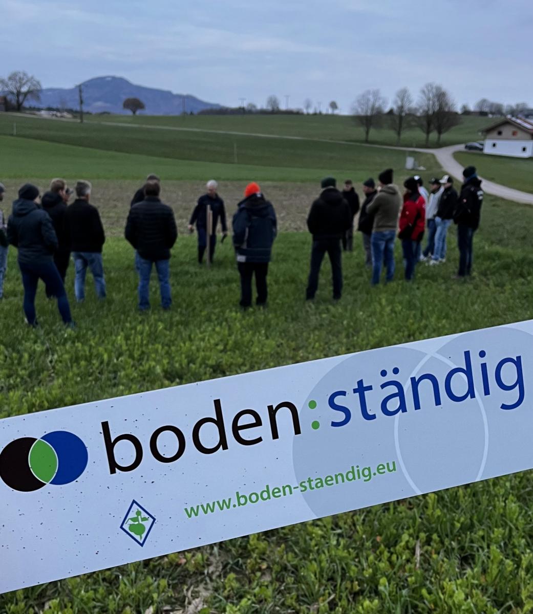 Personen stehen auf einem Feld, zwei Personen erklären etwas
