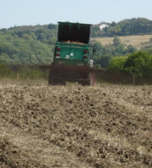 Ein Miststreuer von hinten, der über einen Acker fährt