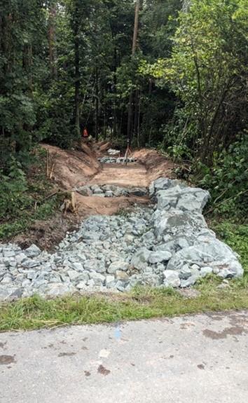 Dargestellt ist eine modellierte Abflußmulde mit einer Steinschüttung aus groben Wasserbausteinen im Wald